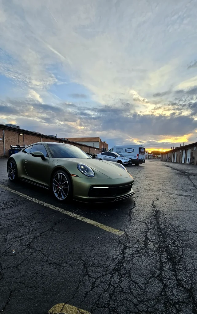 Satin green Porsche 911 color-change wrap under a sunset sky
