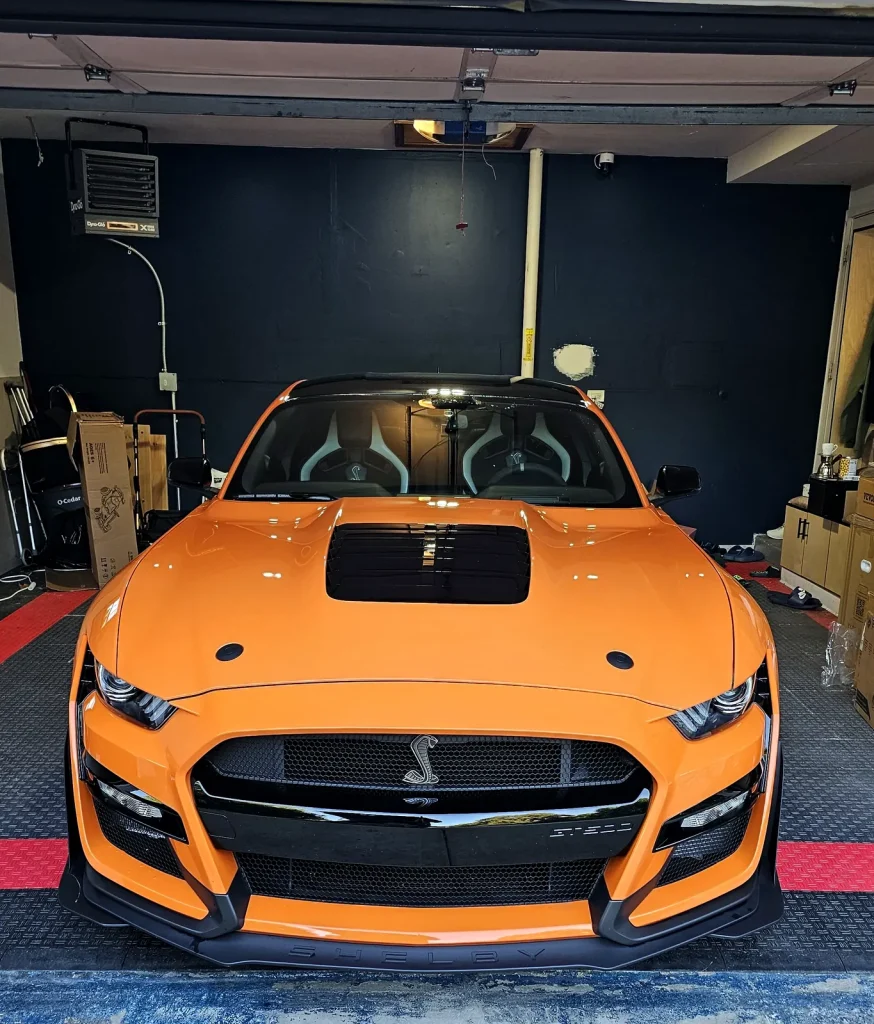 Orange Shelby GT500 with black vinyl racing stripes, three-quarter view
